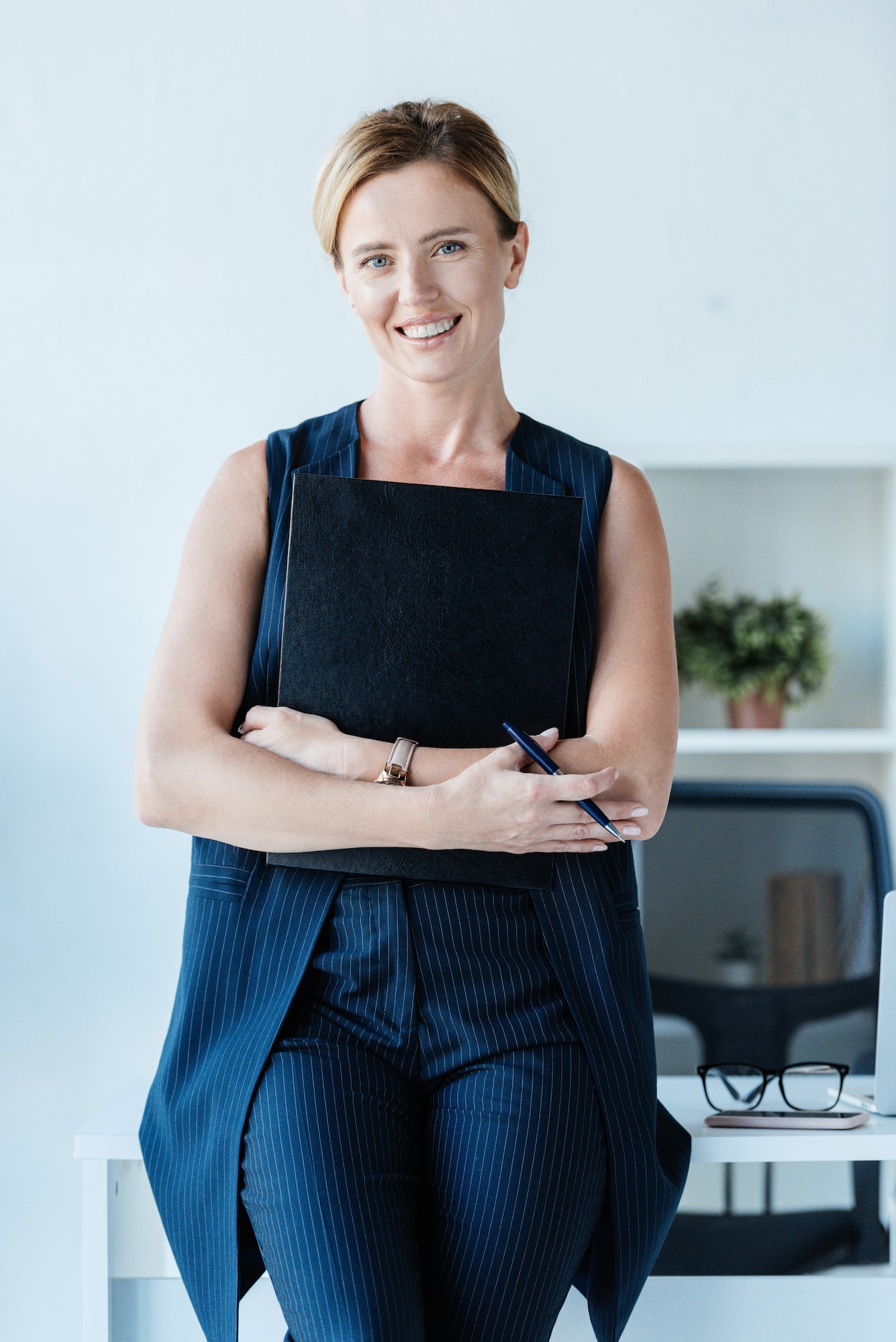 happy adult businesswoman holding folder and pencil near table in office 1